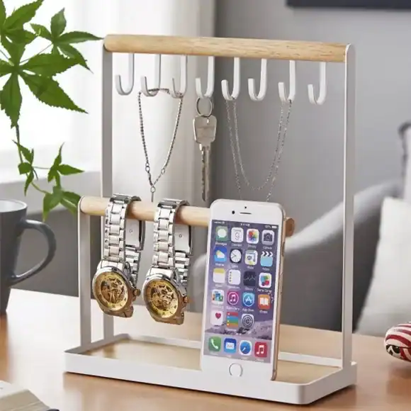Metal jewelry and watch display organizer with phone holder on wooden desk.