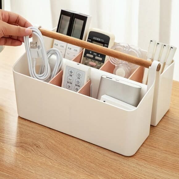 Multi-compartment white desk organizer with wooden handle, neatly holding remotes, cables, and stationery on a wooden table