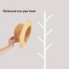 Hand holding a straw sunhat against minimalist white coat rack, modern home decor scene.