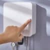 A hand pressing the pop-button to open the wall-mounted key box, with a zoomed-in view of the locking mechanism.